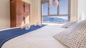 Habitación de hotel con cama, armario de madera y vistas a las montañas a través de amplios ventanales.