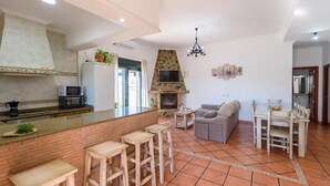 Een moderne keuken met een keukeneiland van baksteen, barstoelen, een eethoek met tafel en stoelen, een open haard en een televisie.
