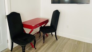 Une pièce avec un bureau rouge, deux chaises noires, un téléviseur à écran plat accroché au mur et une porte.
