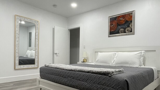 Une chambre moderne avec un grand lit, un miroir, un tableau et une porte donnant sur une autre pièce.