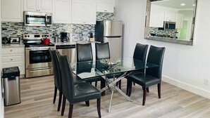Une cuisine moderne avec des armoires blanches, des appareils en acier inoxydable, une table à manger en verre avec des chaises noires et un grand miroir au mur.