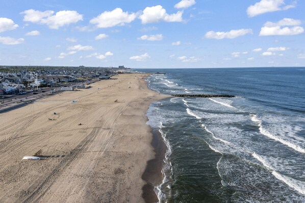 A beach with a pier, a sandy shore, and a residential area in the background.