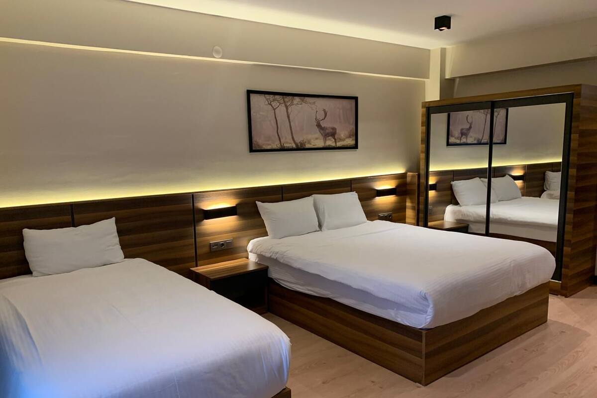A hotel room with two beds, wooden headboards, bedside tables, and a large mirror.