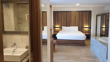 Una habitación de hotel moderna con una cama grande, un baño con lavamanos y espejo, y suelo de madera.