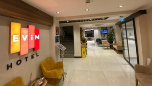 Un hall de hotel con mostrador de recepción, un televisor y una escalera que lleva a los pisos superiores.