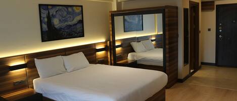 A modern hotel room with a large bed, wooden headboard, bedside tables, a nightstand, a mirror, and a painting on the wall.