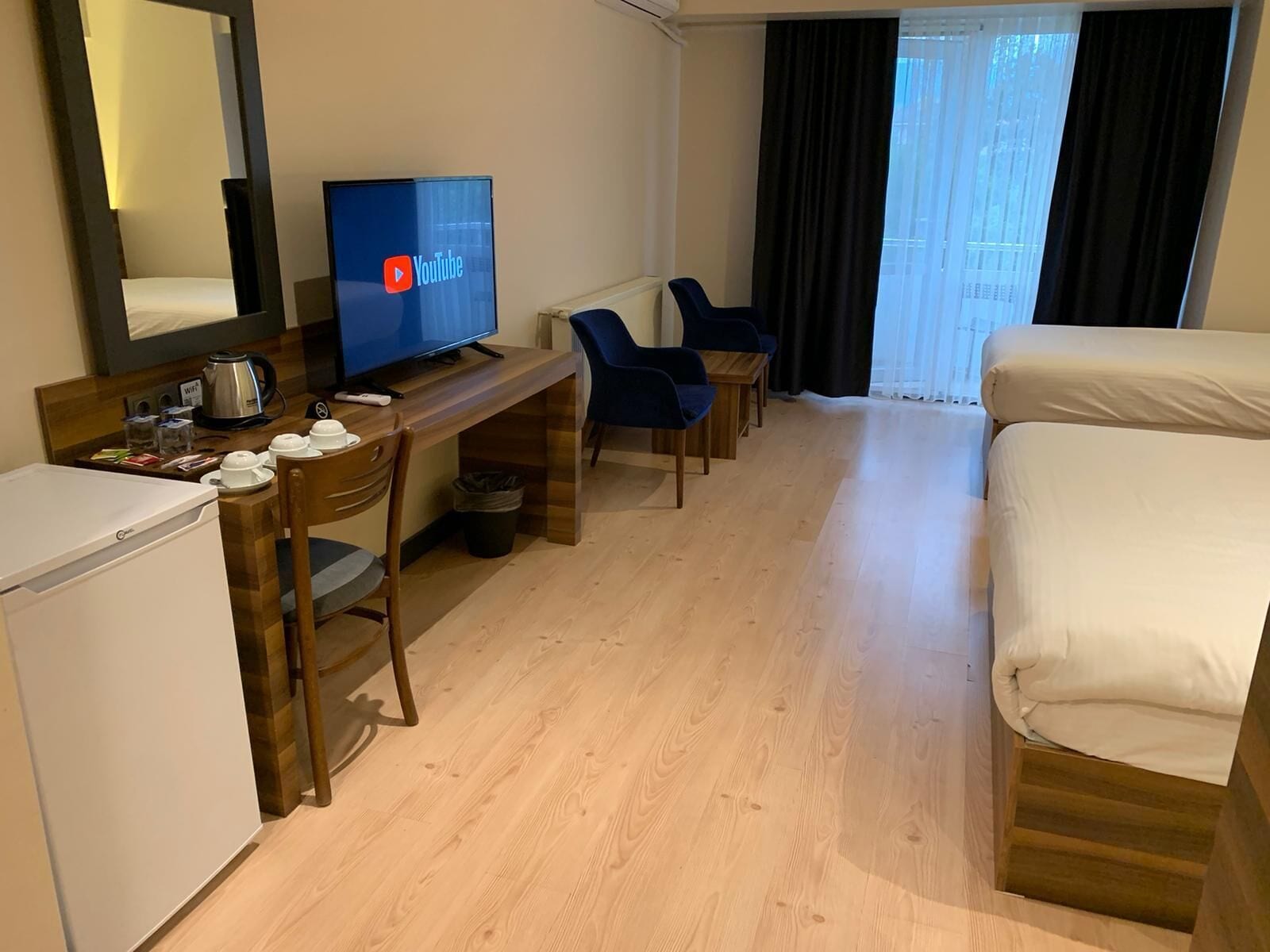 A hotel room with a bed, a desk with a computer, a coffee maker, and a TV displaying the YouTube logo.