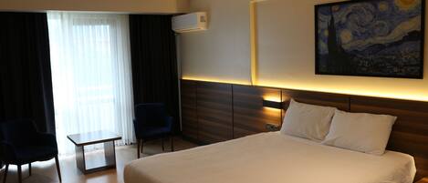 A hotel room with a large bed, a desk, a chair, and a painting on the wall.
