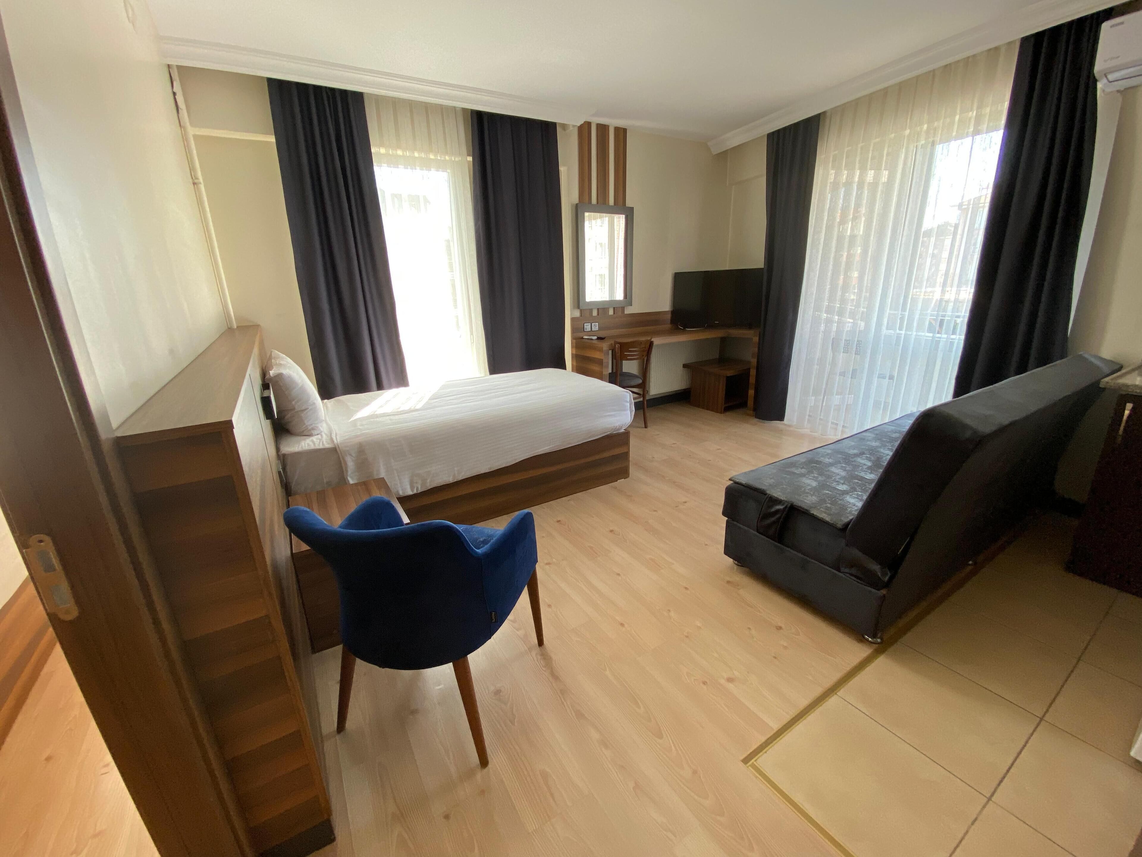 A hotel room with a bed, a desk, a chair, a sofa, and a television.