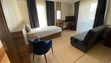 A hotel room with a bed, a desk, a chair, a sofa, and a television.