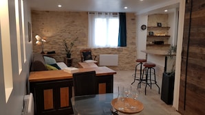 A cozy dining area with a wooden table and chairs, a stone wall, and a window with curtains. - Quiet house in the countryside (CADEROUSSE)