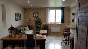 A cozy living room with a stone wall, a wooden dining table, a sofa, a coffee table, and a potted plant.