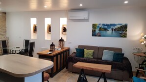 A modern living room with a glass dining table, a brown sofa with cushions, a wooden coffee table, and a painting of a landscape on the wall. - Quiet house in the countryside (CADEROUSSE)