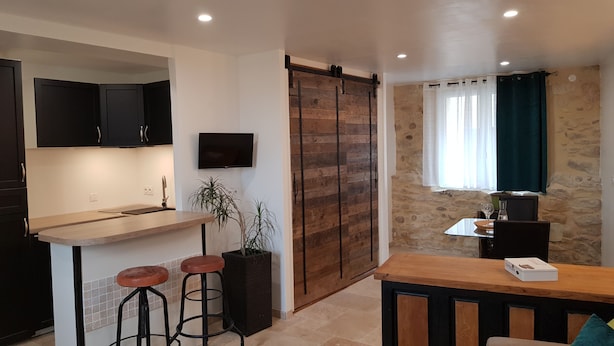A modern kitchen with a wooden island, black cabinets, and a TV mounted on the wall. - Quiet house in the countryside (CADEROUSSE)