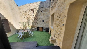 A courtyard with a wooden deck, a table with chairs, and a stone wall. - Quiet house in the countryside (CADEROUSSE)