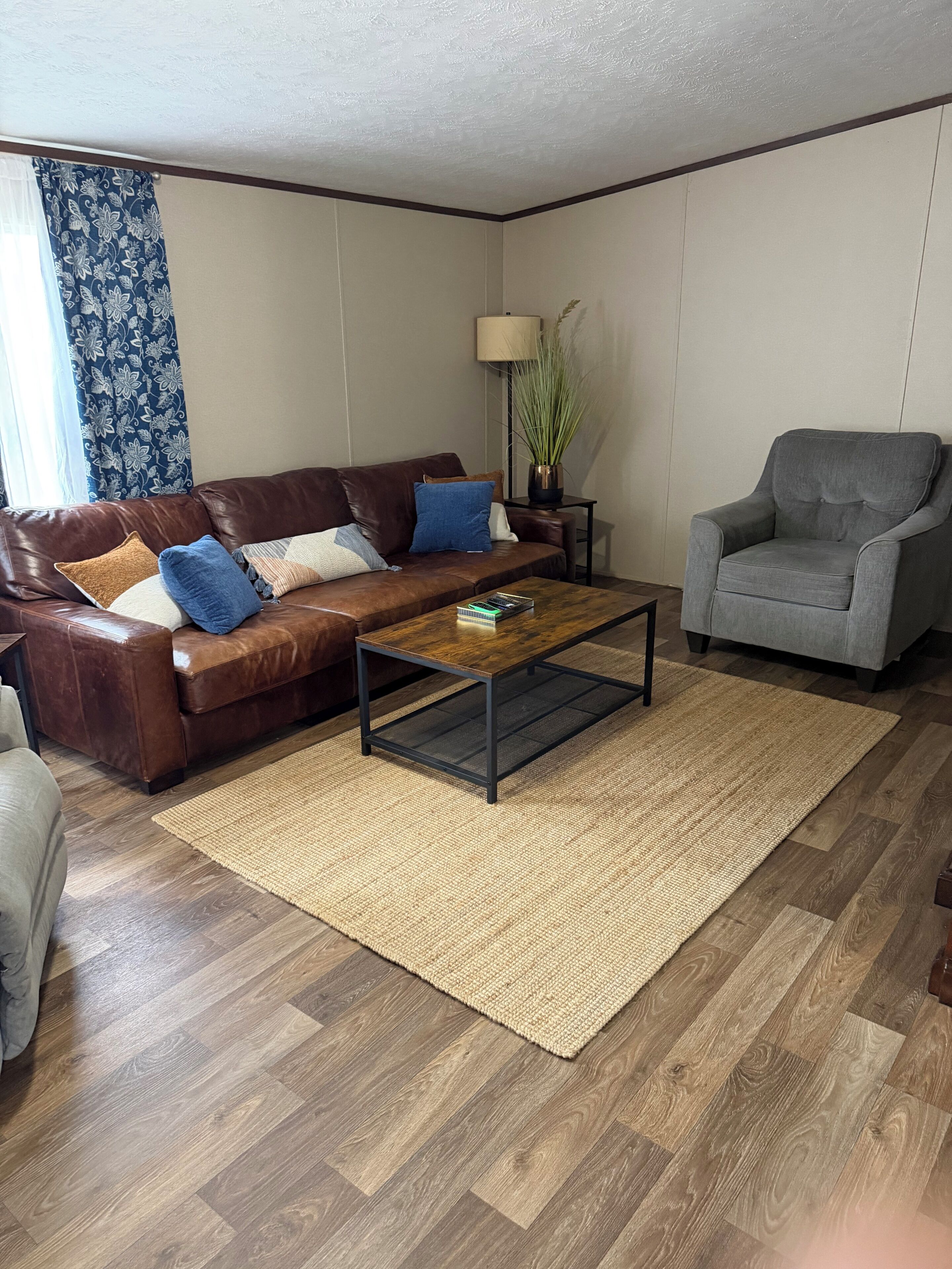 Una sala de estar con un sofá de cuero marrón, un sillón gris, una mesa de centro de madera y una lámpara de pie.