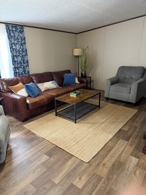 A living room with a brown leather sofa, a grey armchair, a wooden coffee table, and a floor lamp.