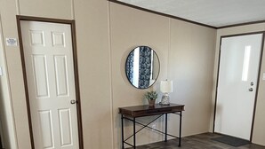 Ein Zimmer mit Holzboden im Fischgrätmuster, einem runden Spiegel an der Wand und einem kleinen Tisch mit Lampe und Pflanze.
