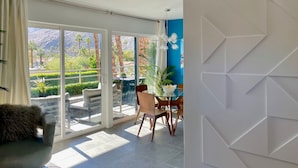 Una sala de estar moderna con un ventanal que da a un balcón, un comedor con mesa y sillas, y vistas a montañas y vegetación.