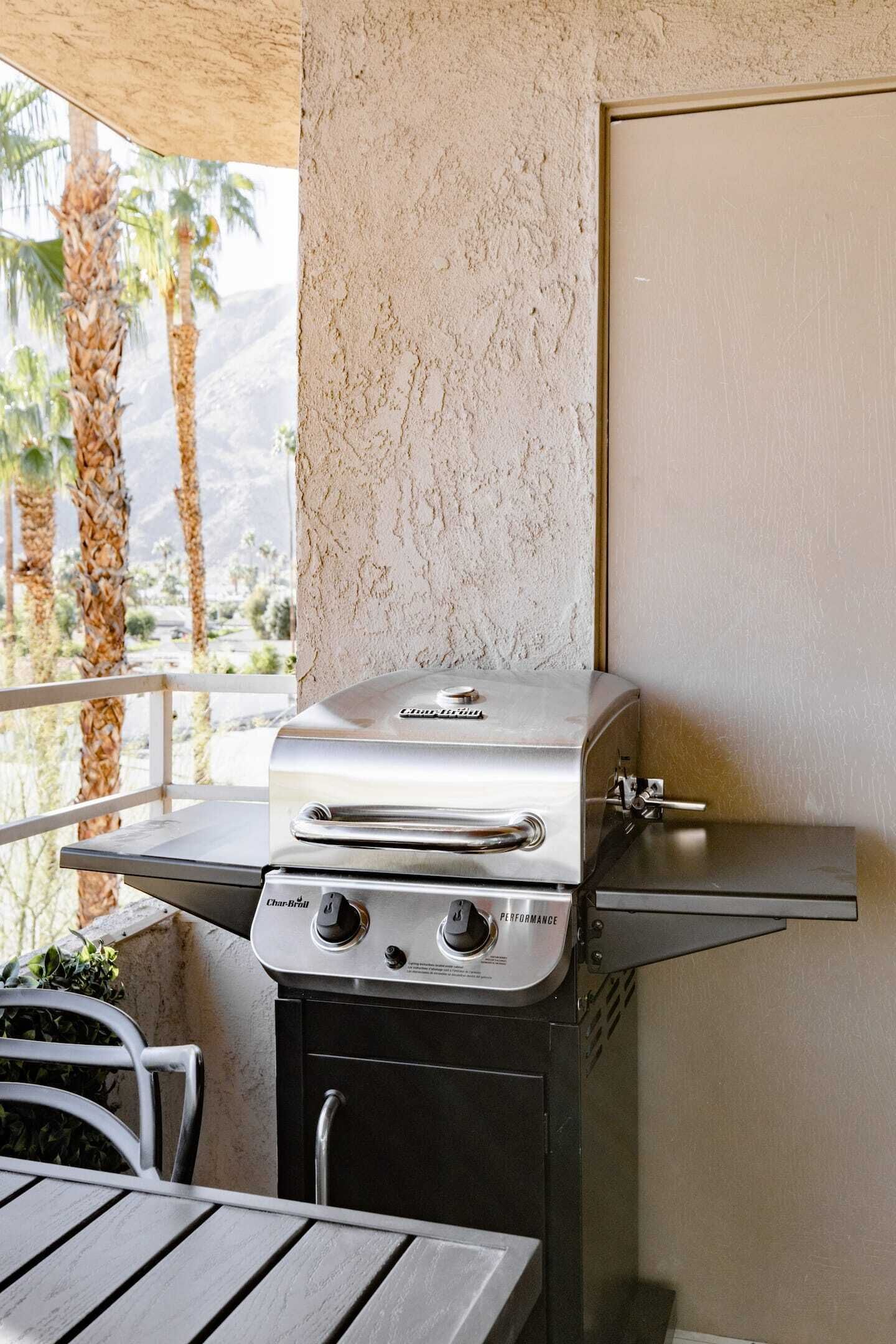 Un barbecue doté d’un panneau de commande, d’une table en métal et offrant une vue sur des palmiers.
