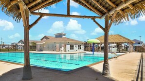 Una piscina con muelle de madera y una estructura techada de paja.