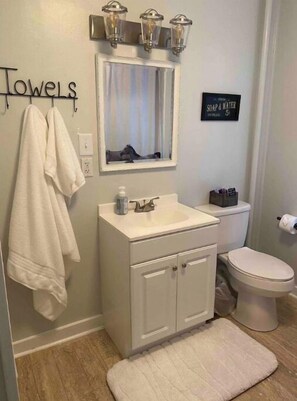 Une salle de bain avec un lavabo blanc, un miroir, un porte-serviettes, des toilettes et un panneau indiquant la présence de savon et d’eau.