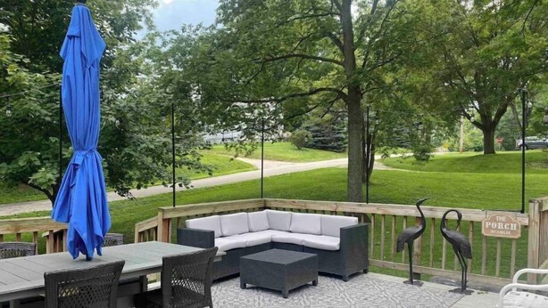 Une terrasse dotée de mobilier d’extérieur, d’un parasol bleu et d’une pancarte indiquant : « Asseyez-vous et détendez-vous sur la véranda ».