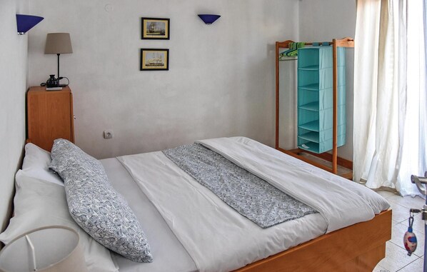 Ein Schlafzimmer mit einem Bett, einem Nachttisch, einer Lampe, zwei gerahmten Bildern und einer blauen Regalwand.