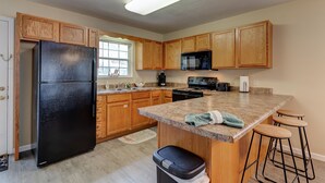 Una cocina con armarios de madera, un refrigerador negro, un microondas, una estufa y una encimera de granito.
