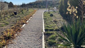 A gravel path leading through a landscaped area with a variety of plants and a small table with chairs. - Apartment between lake and sea amidst vineyards (Peret)