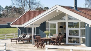 Een overdekt terras met een tafel, stoelen en een bankje, inclusief een bloevas.