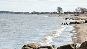 Een strand met een rotsachtige kustlijn en rustig water.