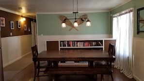 Un comedor con una mesa de madera y bancos, una estantería llena de libros y una lámpara colgante.