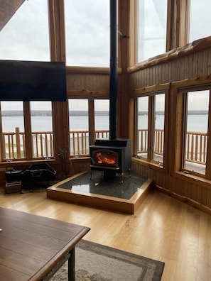 Cozy cabin-style room with a large fireplace, wooden floor, and expansive lake views.