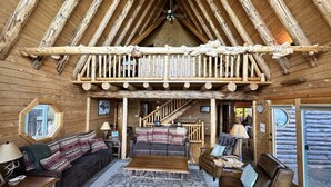 Interior de una cabaña de troncos con un dormitorio en el altillo, muebles de madera y decoración rústica.