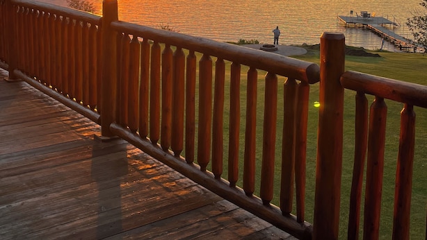 Una terraza de madera con barandilla que da a un cuerpo de agua al atardecer.