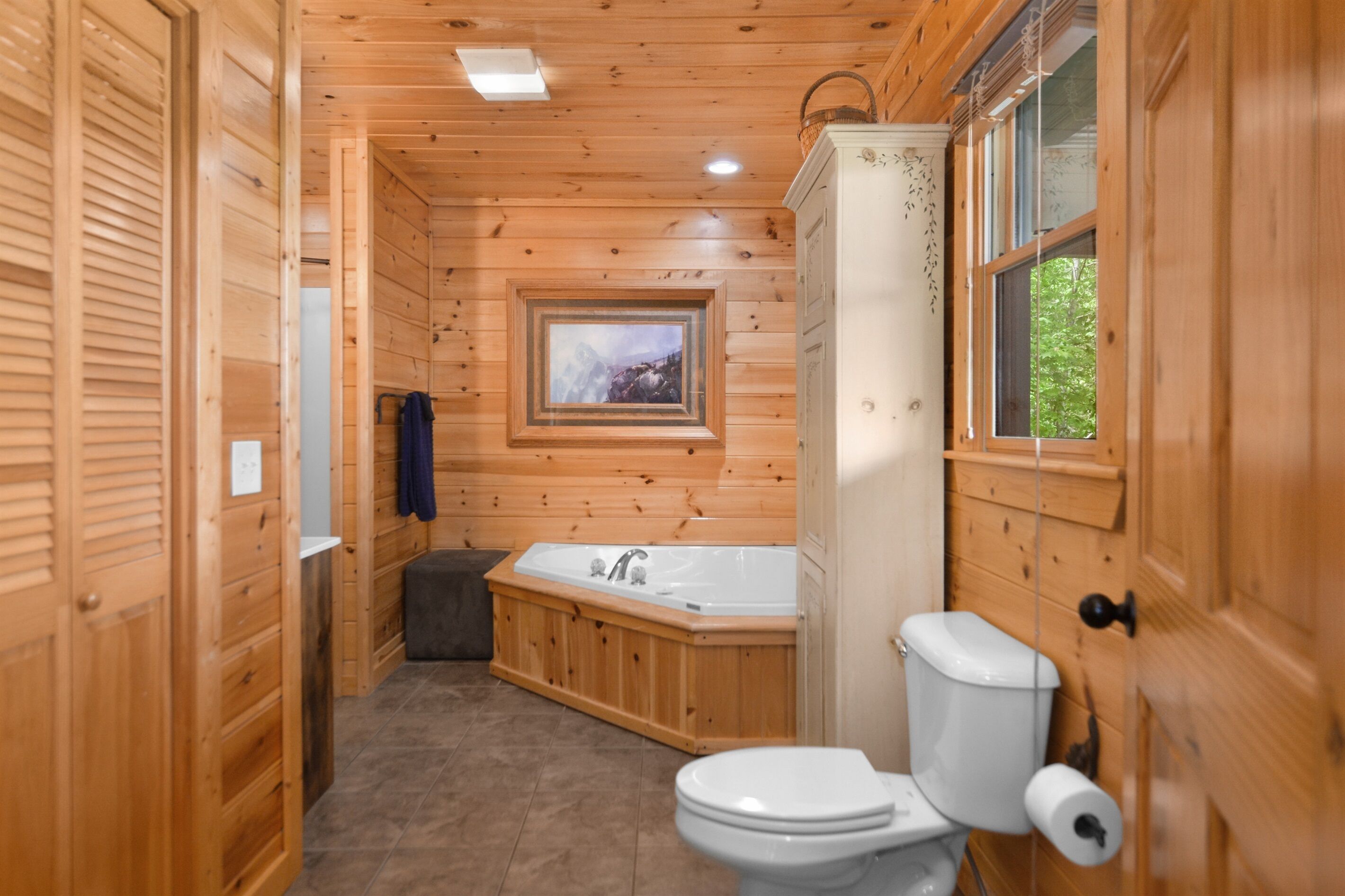 Une salle de bain rustique, avec une cabine en bois, une baignoire en bois, des toilettes et un tableau encadré au mur.