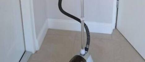 A standing vacuum cleaner in a hallway with white walls and a tiled floor.
