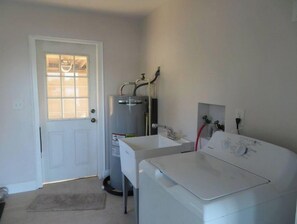 Ett kompakt tvättrum med en tvättmaskin och en torktumlare som båda har frontmatning, en varmvattenberedare och ett fönster med persienner.