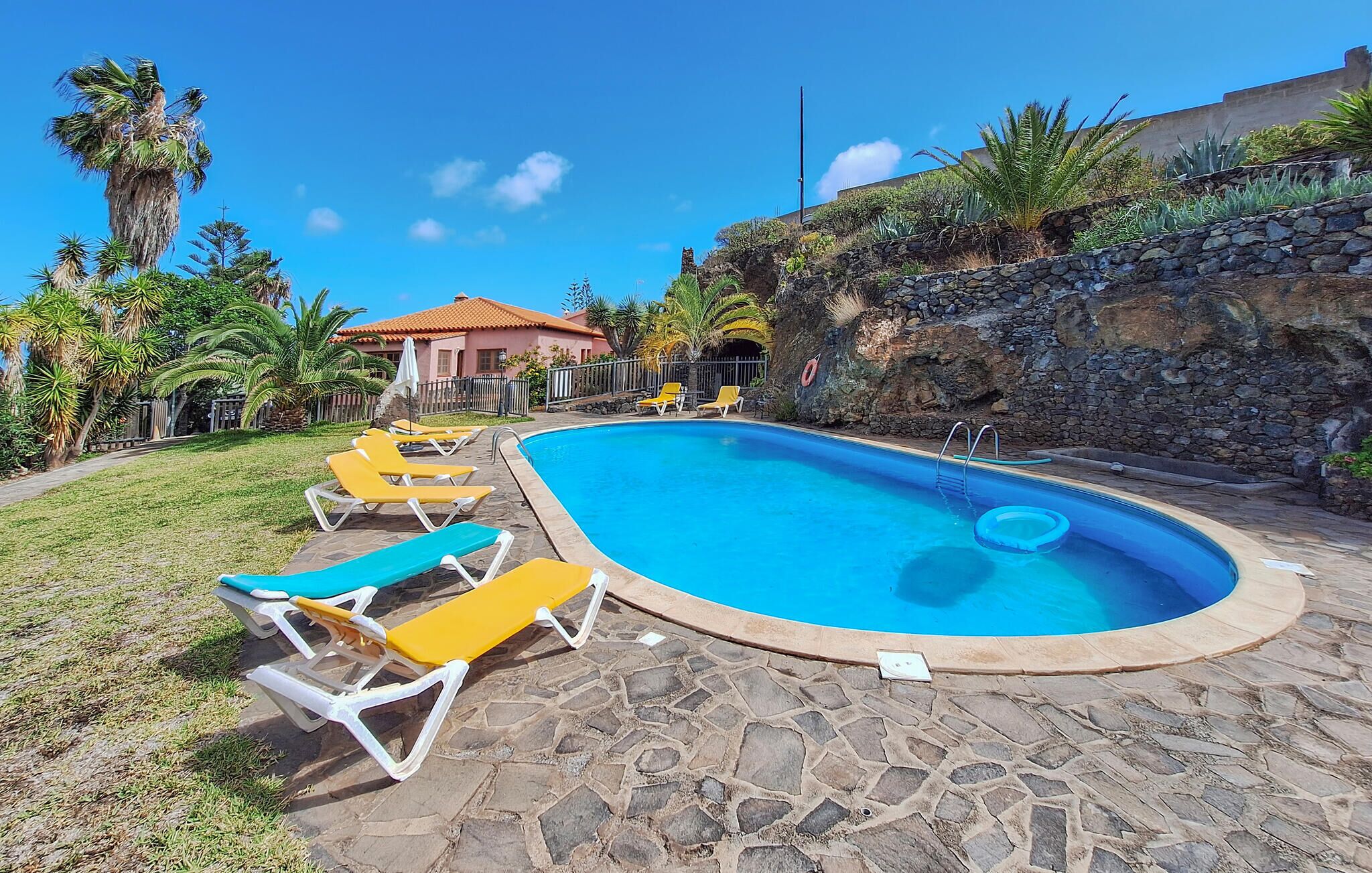 Una piscina con sillas de descanso, un sendero de piedra y un muro de piedra con vegetación.