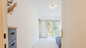 A hallway leading to a bedroom with a large window, a ceiling light fixture, and a wardrobe with dark handles. - Renovated 3-Room Apartment in a Leafy Park (Cannes)