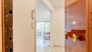 A hotel room with a marble floor, a wooden door with a brass handle, and a view of an outdoor dining area with tables and chairs. - Renovated 3-Room Apartment in a Leafy Park (Cannes)