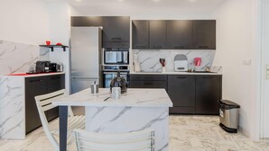 A modern kitchen with marble countertops, a built-in oven, and dark cabinetry. - Renovated 3-Room Apartment in a Leafy Park (Cannes)
