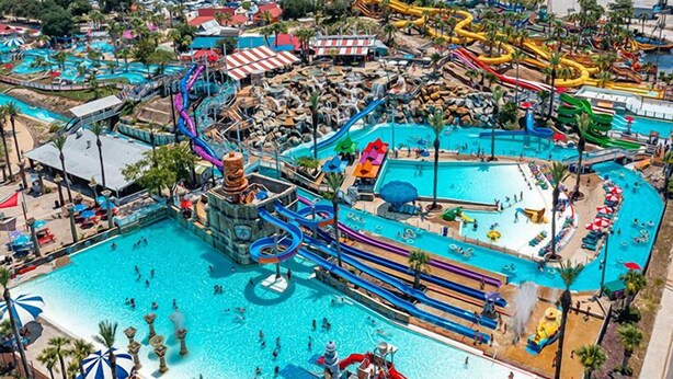 Un gran parque acuático con múltiples piscinas, toboganes y una fuente central de agua.