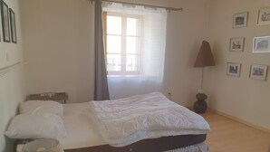 Une chambre à coucher avec un lit, une lampe de chevet, une fenêtre avec des rideaux et des tableaux encadrés accrochés au mur.