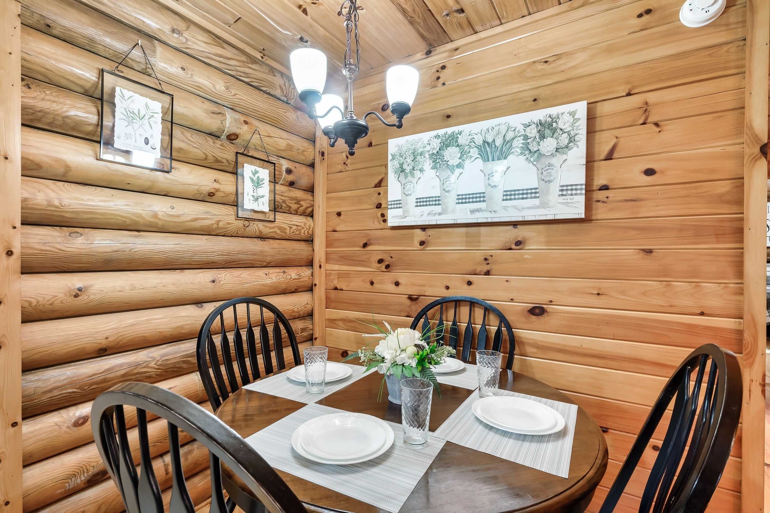 Comedor de una cabaña de madera con una mesa redonda, sillas negras e impresiones botánicas enmarcadas en las paredes.
