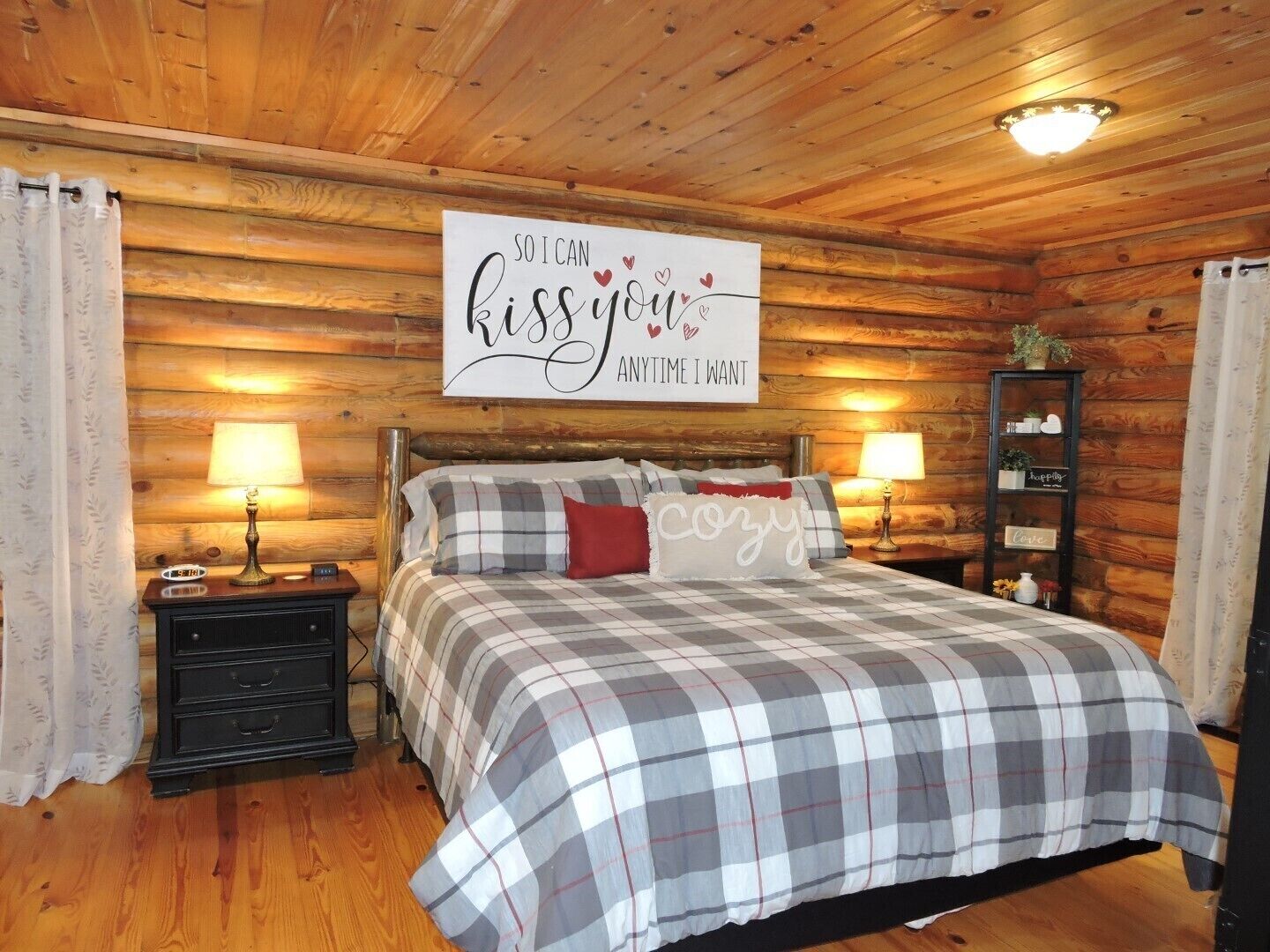 A cozy wooden cabin bedroom with a bed, two bedside tables, a nightstand, and a sign on the wall.