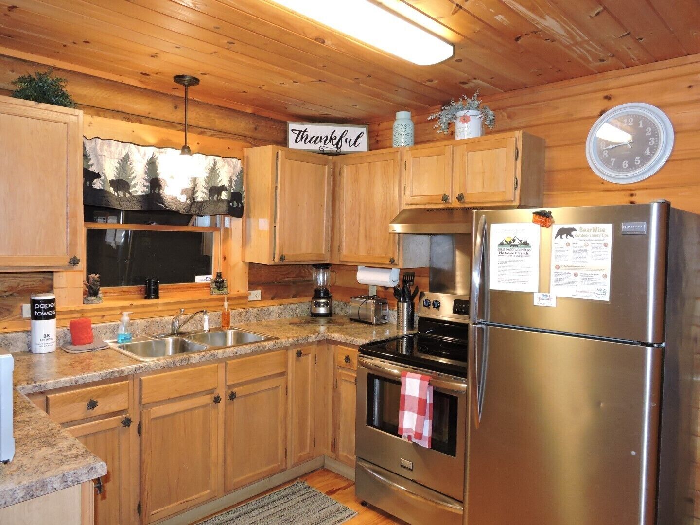 A kitchen with wooden cabinets, a stainless steel refrigerator, a stove, and a clock on the wall.