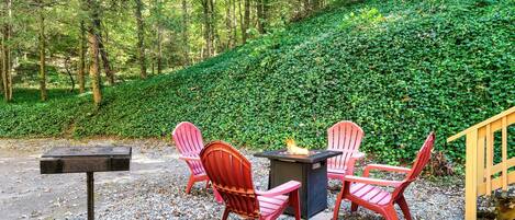 Un área de estar al aire libre con sillas Adirondack rojas, una mesa de metal y un brasero.