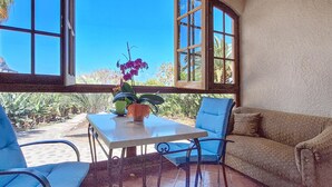 A room with a table and chairs, a sofa, and large windows with a view of palm trees and a clear sky. - 1 bedroom amazing apartment in Buenavista Del Norte (Buenavista Del Norte)